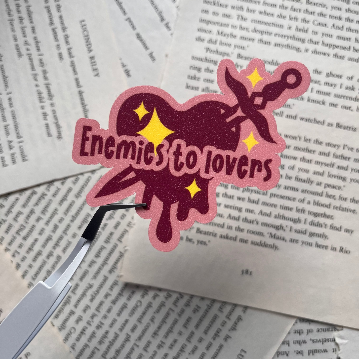 Heart-shaped sticker with 'Enemies to Lovers' text on a book page