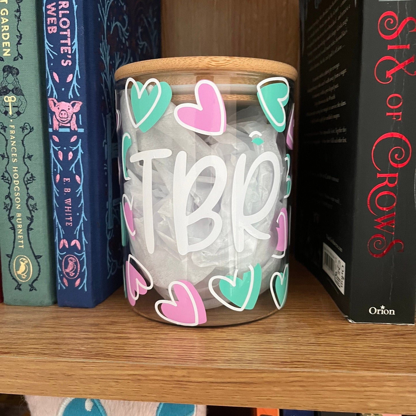 Jar with 'TBR' and heart shapes on a bookshelf with books around