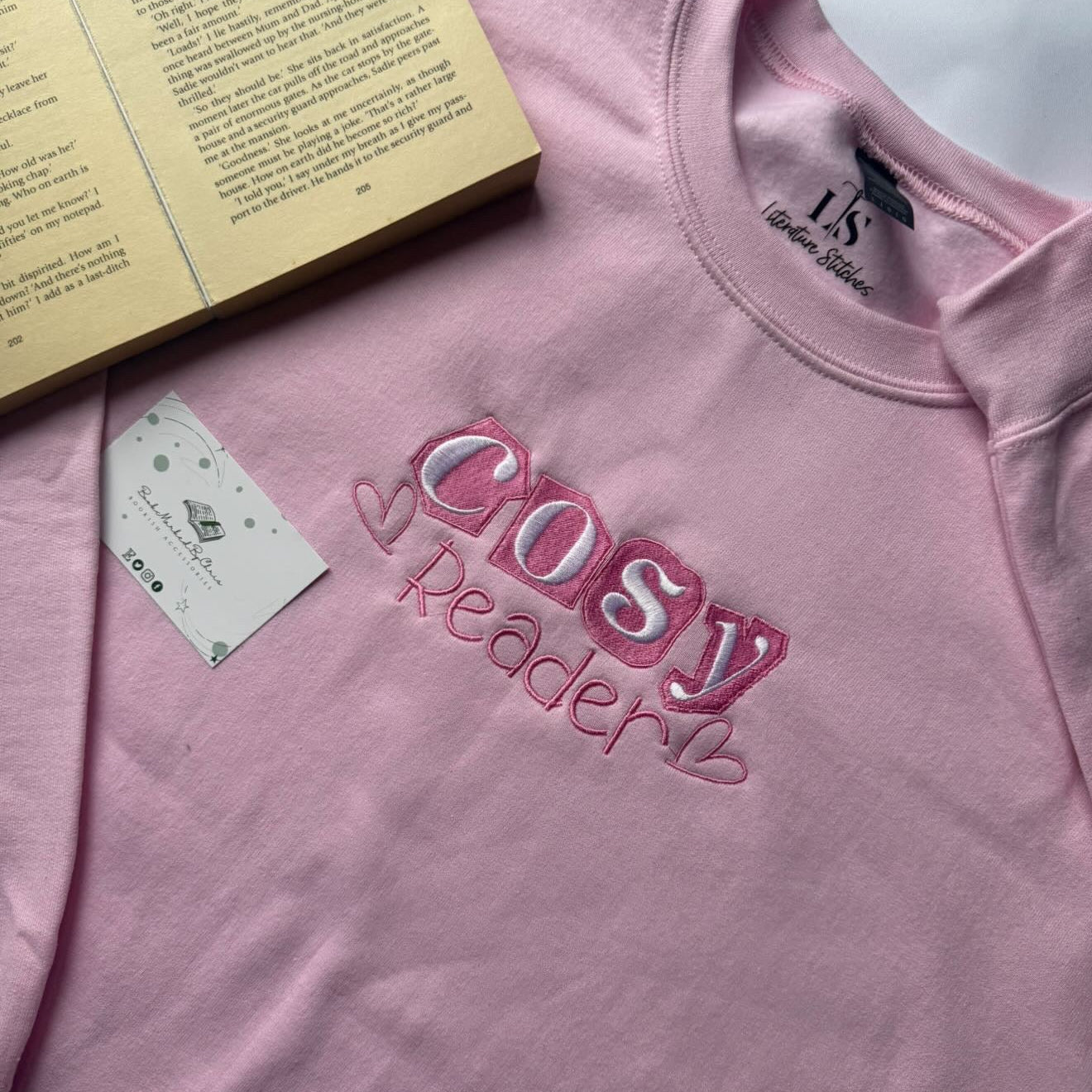 Pink sweatshirt with 'Cosy Reader' text and a book on a light background