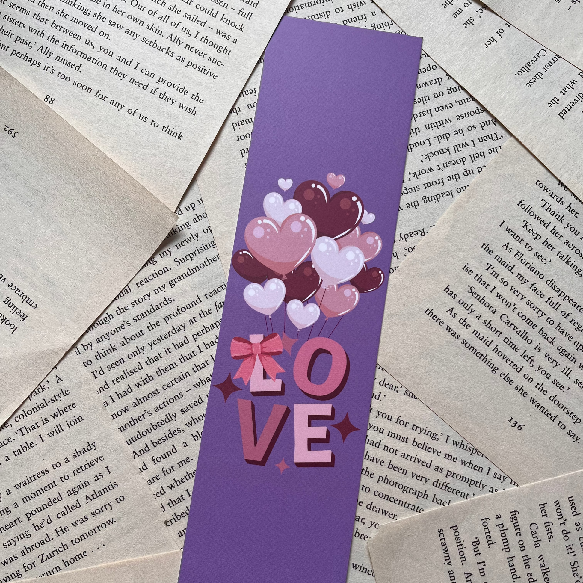 Purple bookmark with heart and 'LOVE' design on a pile of books