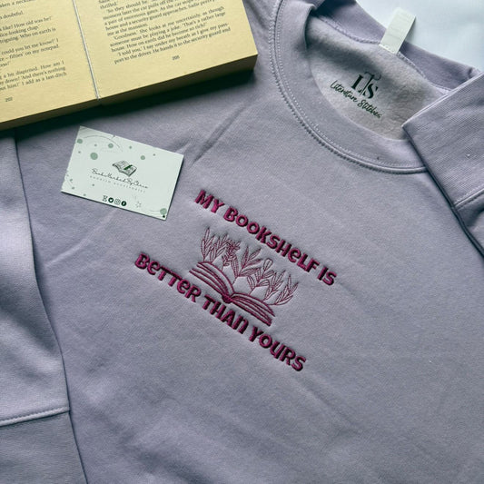 Gray sweatshirt with 'My bookshelf is better than yours' text and a book in the background