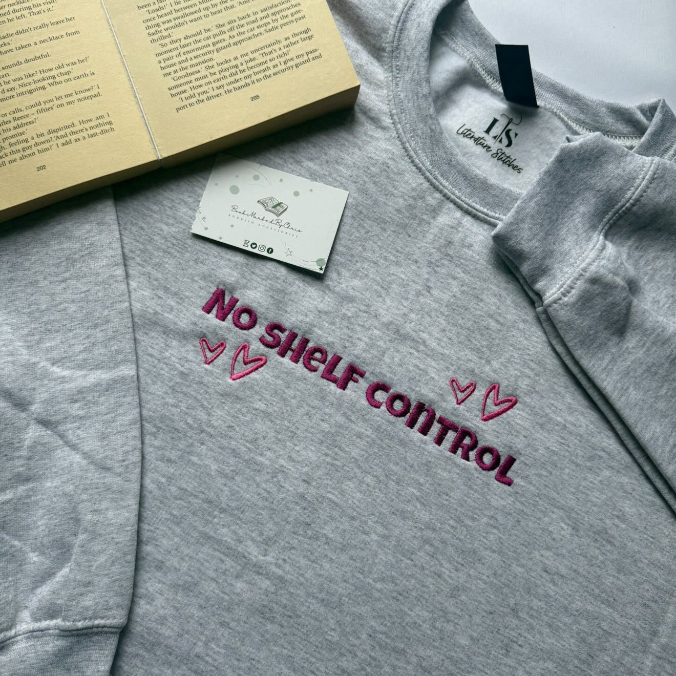 Gray sweatshirt with 'No Shelf Control' text on a white surface