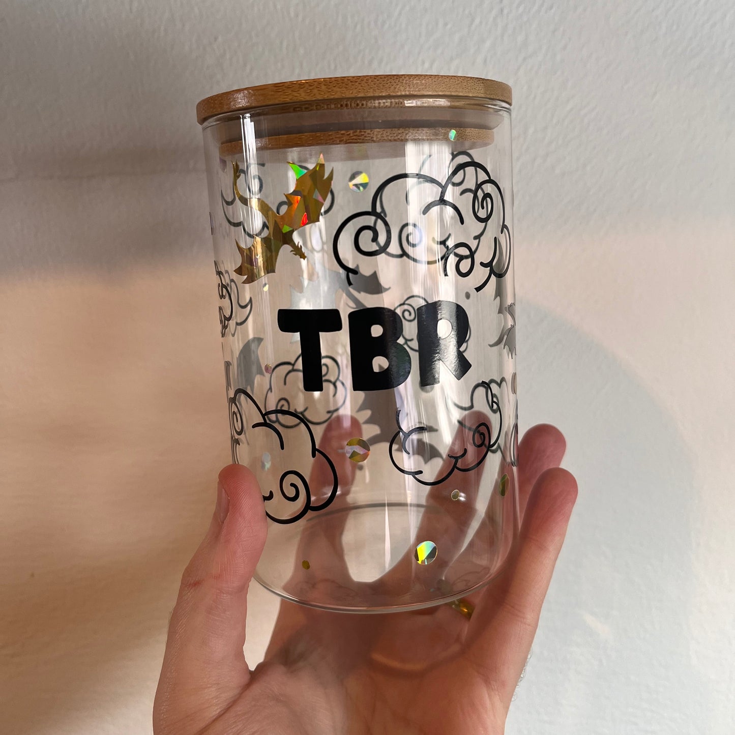 Clear glass tbr jar with wooden lid held by a hand against a neutral background