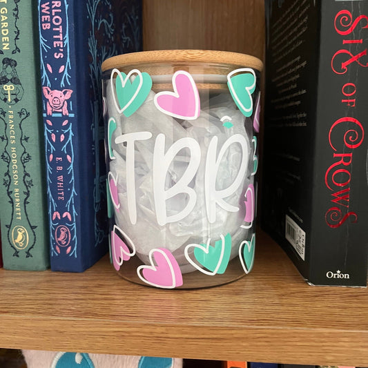 Jar with 'TBR' and heart shapes on a bookshelf with books around