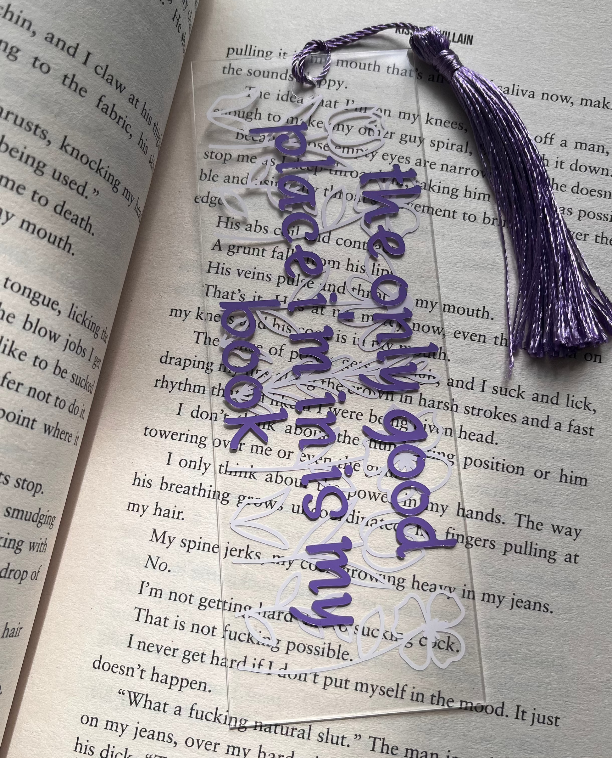 Open book with an acrylic bookmark on it saying " the only good place i'm in is my book" with a floral background