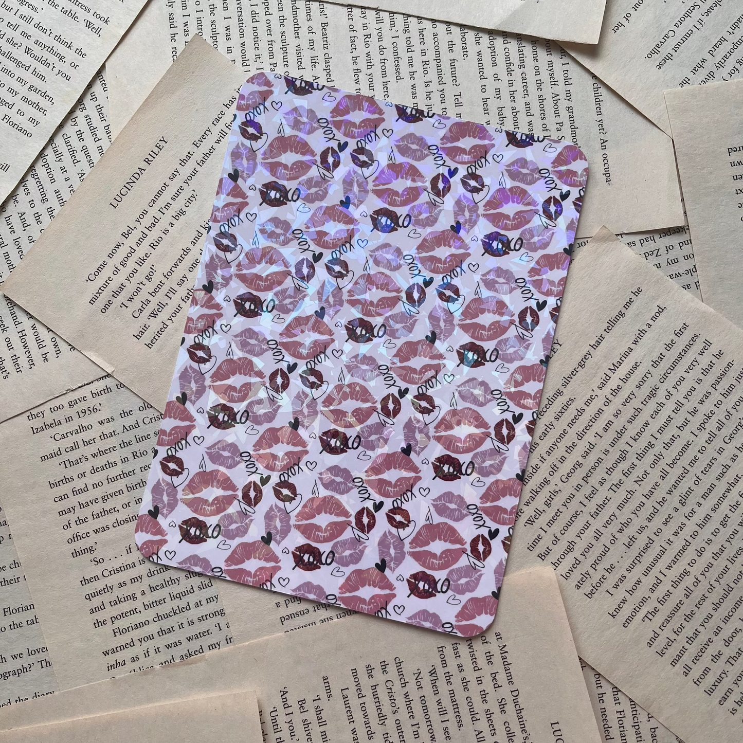 a kindle insert lay on book pages. Kindle insert has a romance theme covered in lipstick kisses and "xoxo"